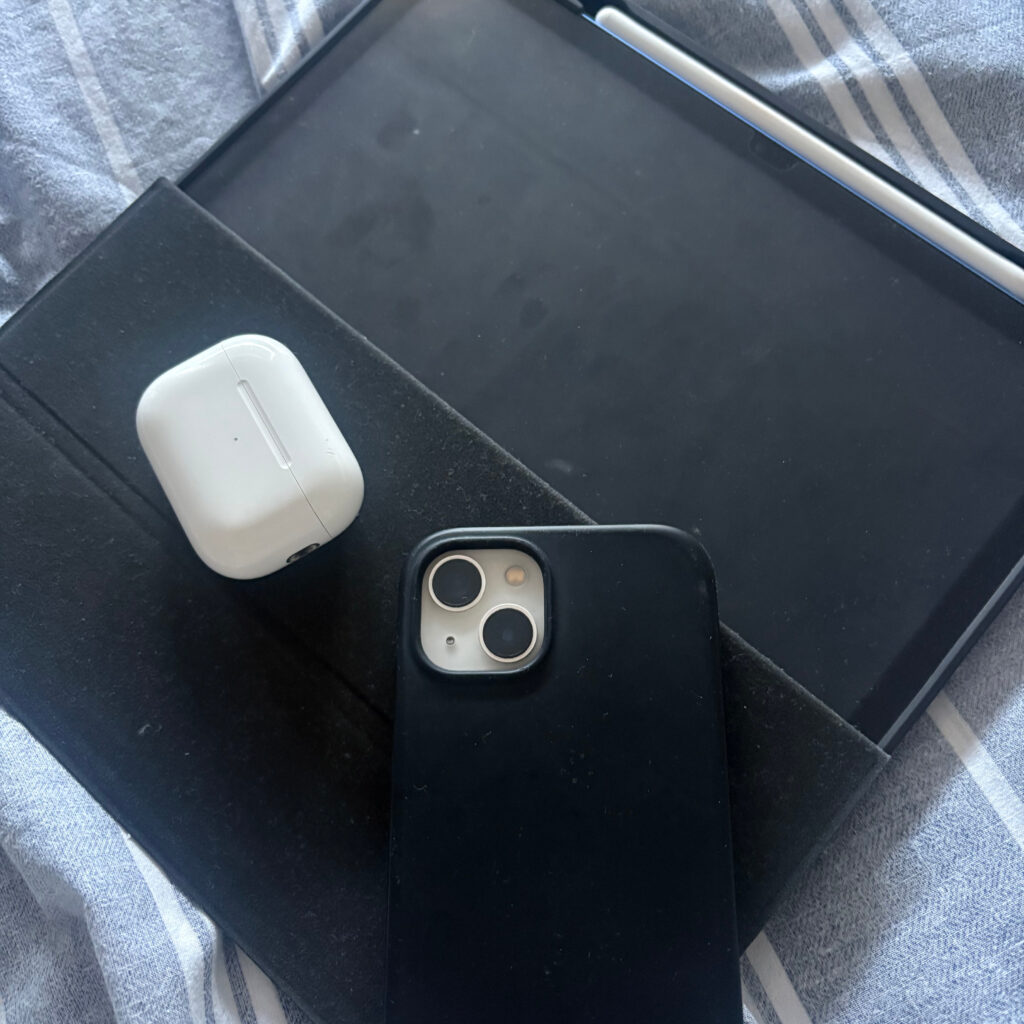 An iPad with the case half open, and AirPods case and iPhone resting on top of the case.