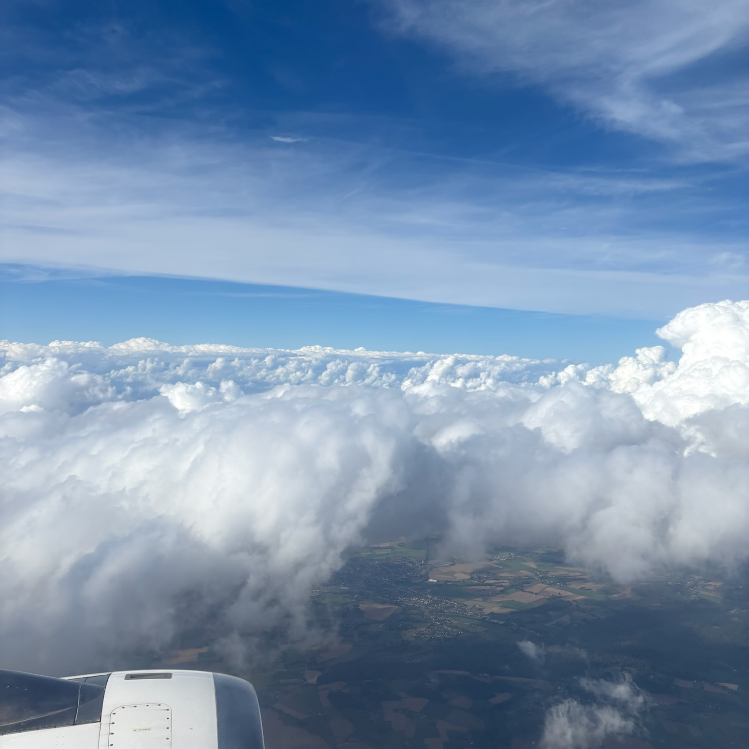 A picture from an aeroplane window, like on a Concorde, of the clouds and the sky above with earth visible at the bottom.